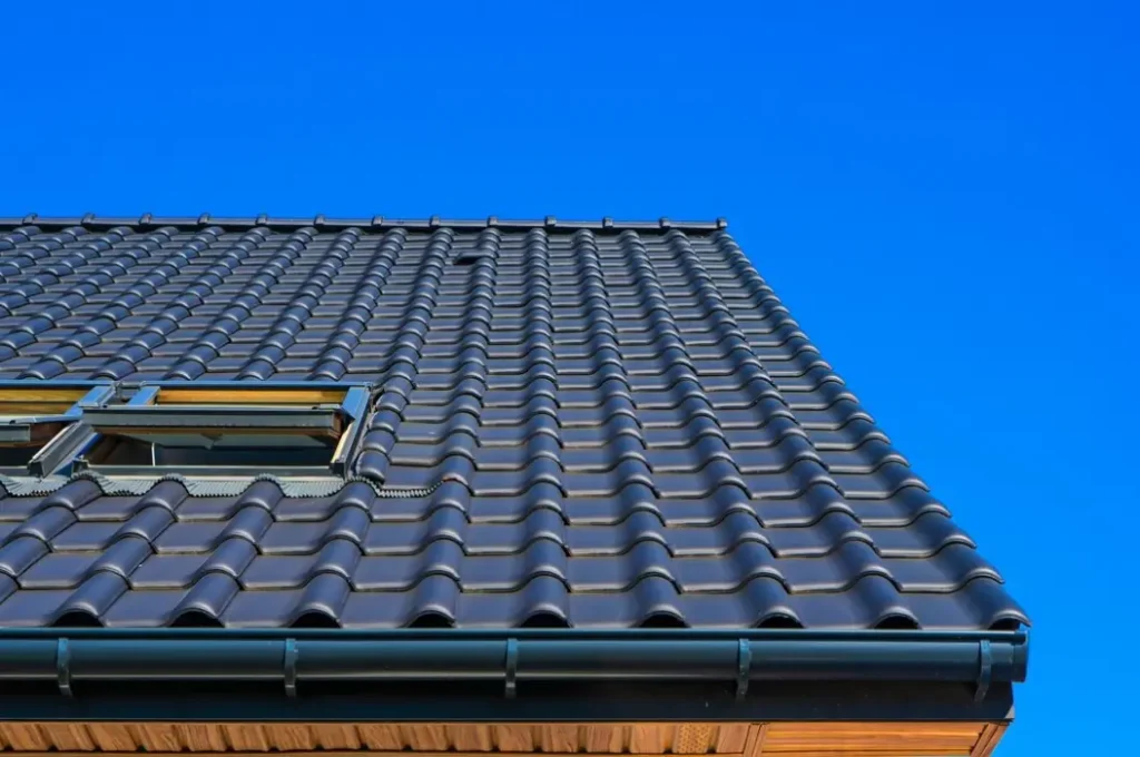 Dark gray tile roof with a skylight against a bright blue sky.